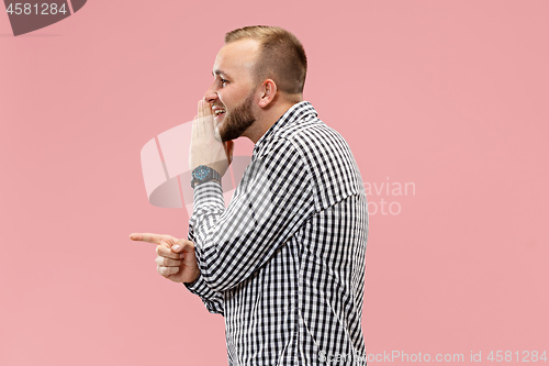 Image of The young man whispering a secret behind her hand over pink background