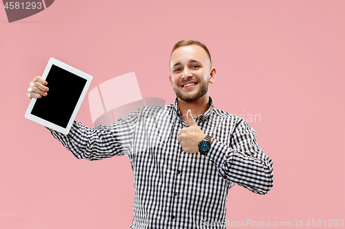 Image of Studio picture of positive man isolated on pink background standing in casual clothes holding tablet and showing it blank screen with happy smile