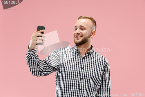 Image of Portrait of attractive young man taking a selfie with his smartphone. Isolated on pink background.