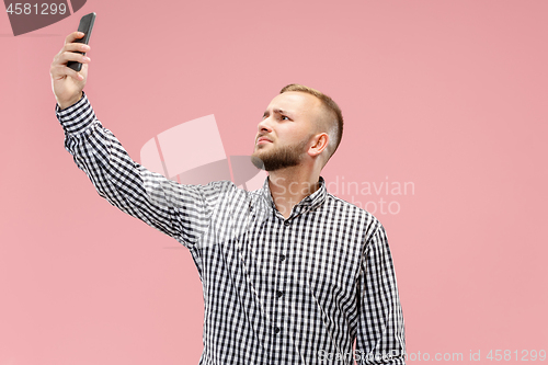 Image of Portrait of attractive young man taking a selfie with his smartphone. Isolated on pink background.