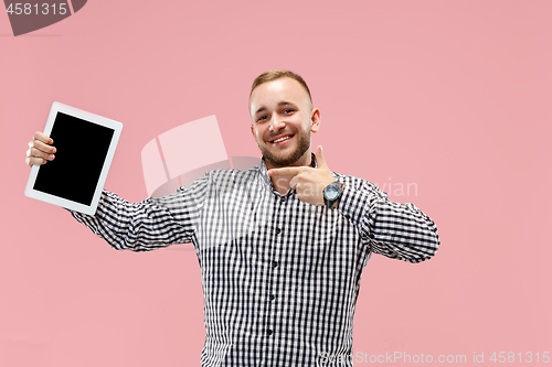 Image of Studio picture of positive man isolated on pink background standing in casual clothes holding tablet and showing it blank screen with happy smile