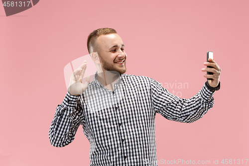 Image of Portrait of attractive young man taking a selfie with his smartphone. Isolated on pink background.