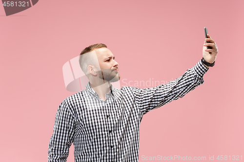 Image of Portrait of attractive young man taking a selfie with his smartphone. Isolated on pink background.