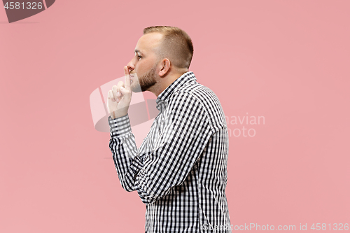 Image of The young man whispering a secret behind her hand over pink background