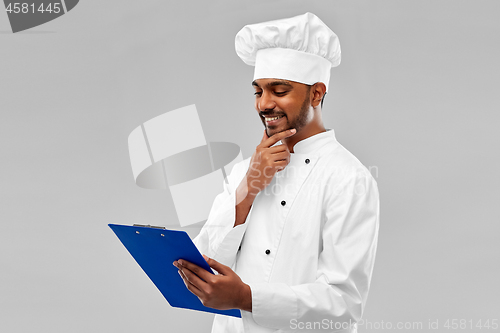 Image of happy indian chef reading menu on clipboard