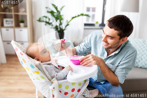 Image of father feeding happy baby in highchair at home