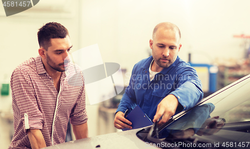 Image of auto mechanic with clipboard and man at car shop