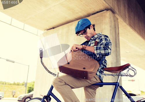 Image of hipster man with bicycle looking something in bag