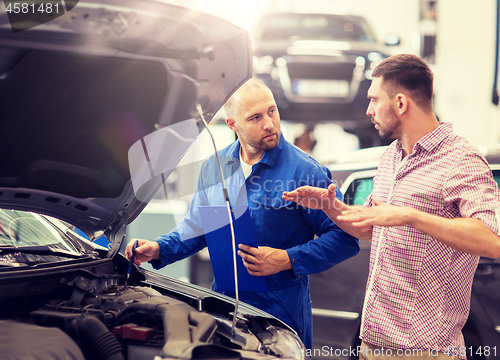 Image of auto mechanic with clipboard and man at car shop