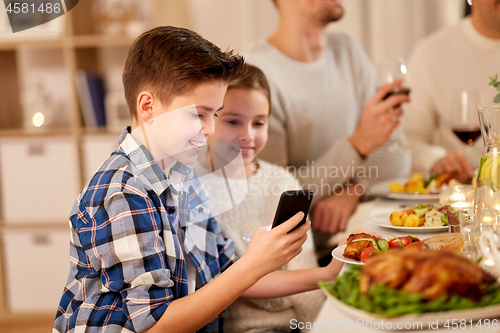 Image of boy with sister using smartphone at family dinner