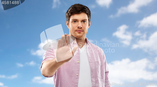 Image of young man showing stop gesture over blue sky