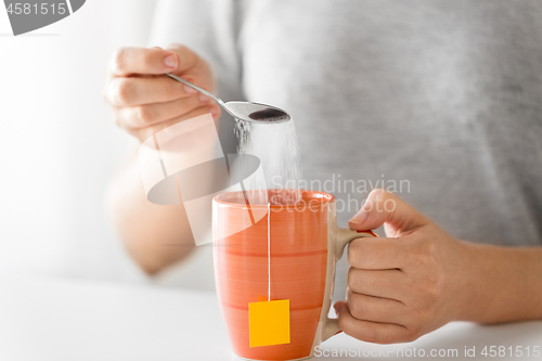 Image of close up of woman adding sugar to cup of tea