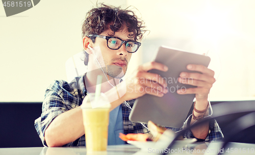 Image of man with tablet pc and earphones sitting at cafe