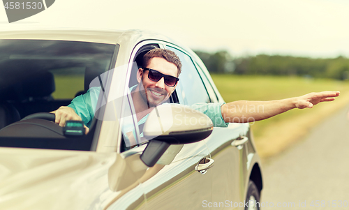 Image of happy man in shades driving car and waving hand