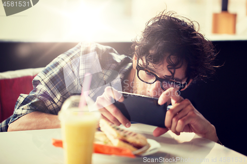 Image of man with smartphone photographing food at cafe