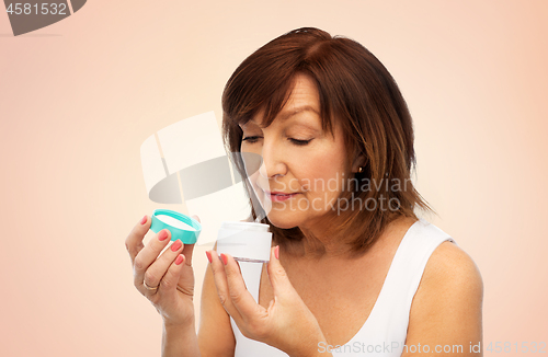 Image of senior woman with cream jar over beige background