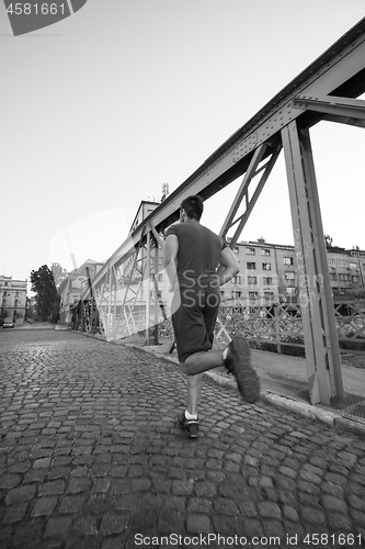 Image of man jogging across the bridge at sunny morning