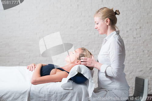 Image of Professional female masseur giving relaxing massage treatment to young female client. Hands of masseuse on forehead of young lady during procedure of spa facial massage