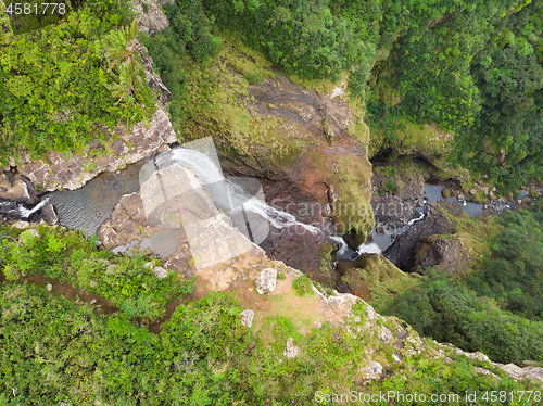 Image of Aerial top view of travel couple waving to drone, standing on the edge of 500 feet waterfall in the tropical island jungle of Black river gorges national park on Mauritius island