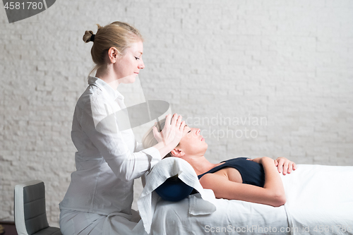 Image of Professional female masseur giving relaxing massage treatment to young female client. Hands of masseuse on forehead of young lady during procedure of spa facial massage