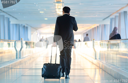 Image of Businessman walking and wheeling a trolley suitcase at the lobby, talking on a mobile phone. Business travel concept.