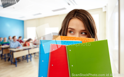 Image of student girl hiding behind notebooks at school