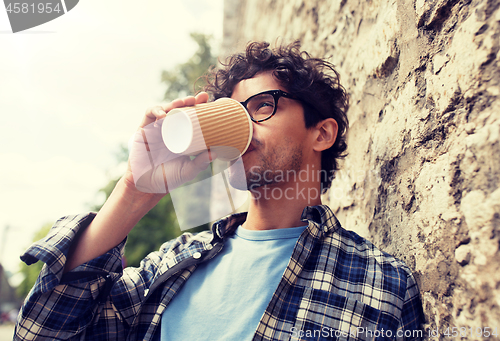 Image of man in eyeglasses drinking coffee over street wall