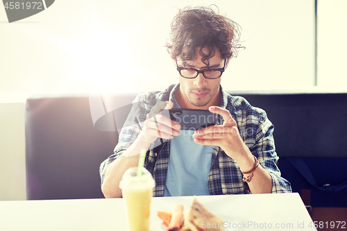 Image of man with smartphone photographing food at cafe