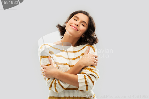 Image of happy woman in striped pullover hugging herself