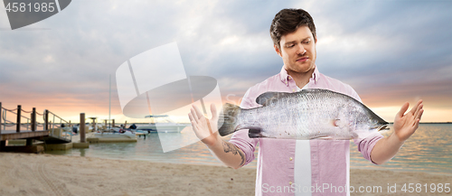 Image of displeased young man showing size of fish on beach