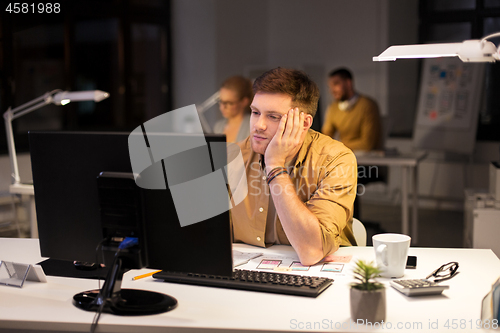 Image of tired or bored man with computer at night office