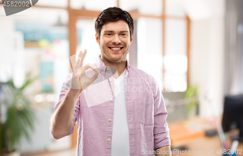 Image of smiling young man showing ok hand sign over office