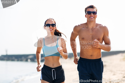 Image of couple in sports clothes running along on beach