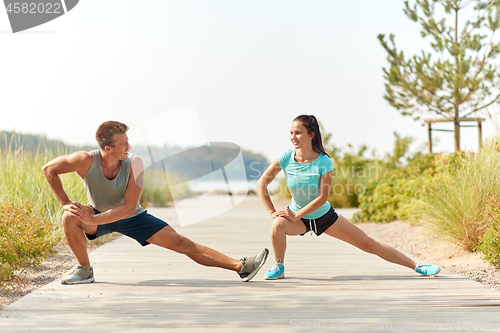 Image of smiling couple stretching legs on beach