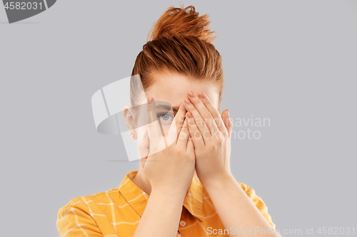 Image of red haired teenage girl looking through fingers