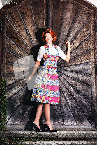 Image of Portrait of a beautiful young woman in a dirndl, standing on a wooden wall.