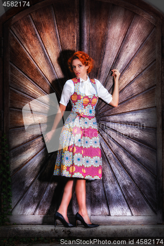 Image of Portrait of a beautiful young woman in a dirndl, standing on a wooden wall.