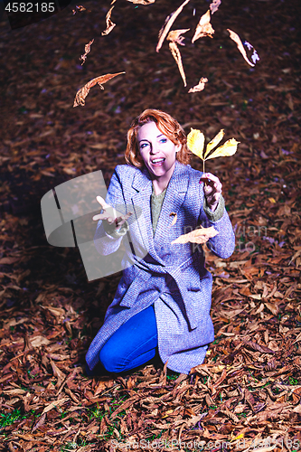 Image of Portrait of a young woman kneeling on the leaves in autumn and throwing this up.