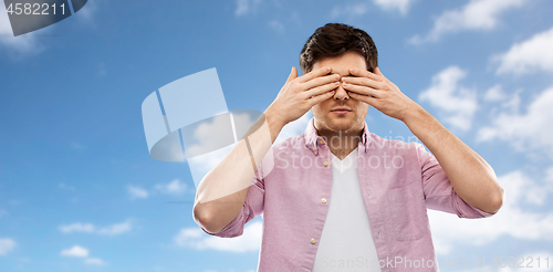 Image of man closing his eyes by hands over blue sky