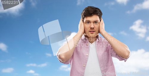 Image of man closing ears by hands over blue sky