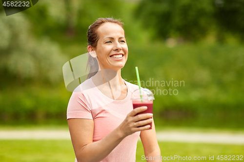 Image of woman drinking smoothie after exercising in park