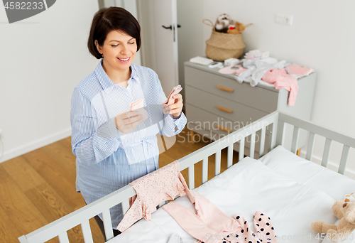 Image of happy pregnant woman setting baby clothes at home