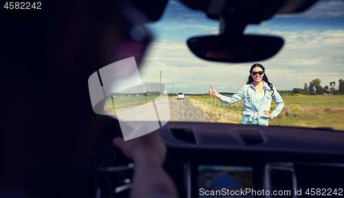 Image of woman hitchhiking and stopping car with thumbs up