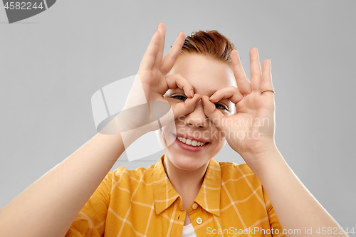 Image of red haired teenage girl making finger glasses