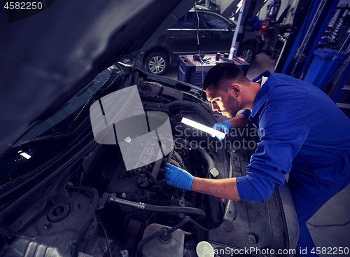 Image of mechanic man with lamp repairing car at workshop