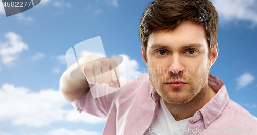 Image of angry young man ready for fist punch over sky