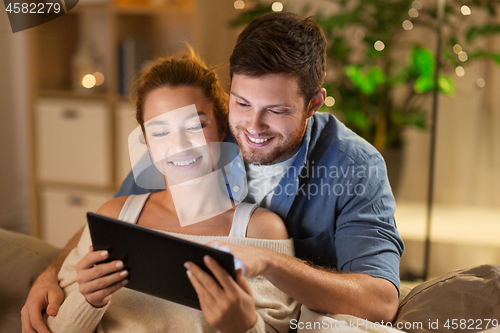 Image of happy couple using tablet pc at home in evening