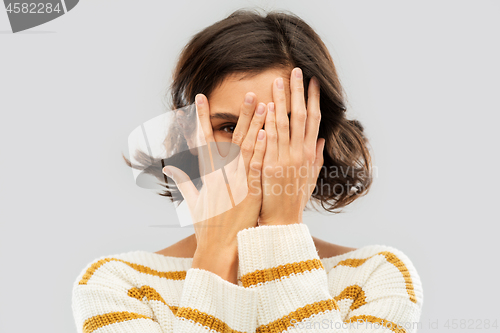 Image of young woman looking by one eye through her fingers