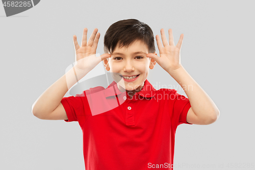 Image of little boy in red t-shirt making big ears by hands