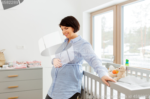 Image of happy pregnant woman next to baby bed at home